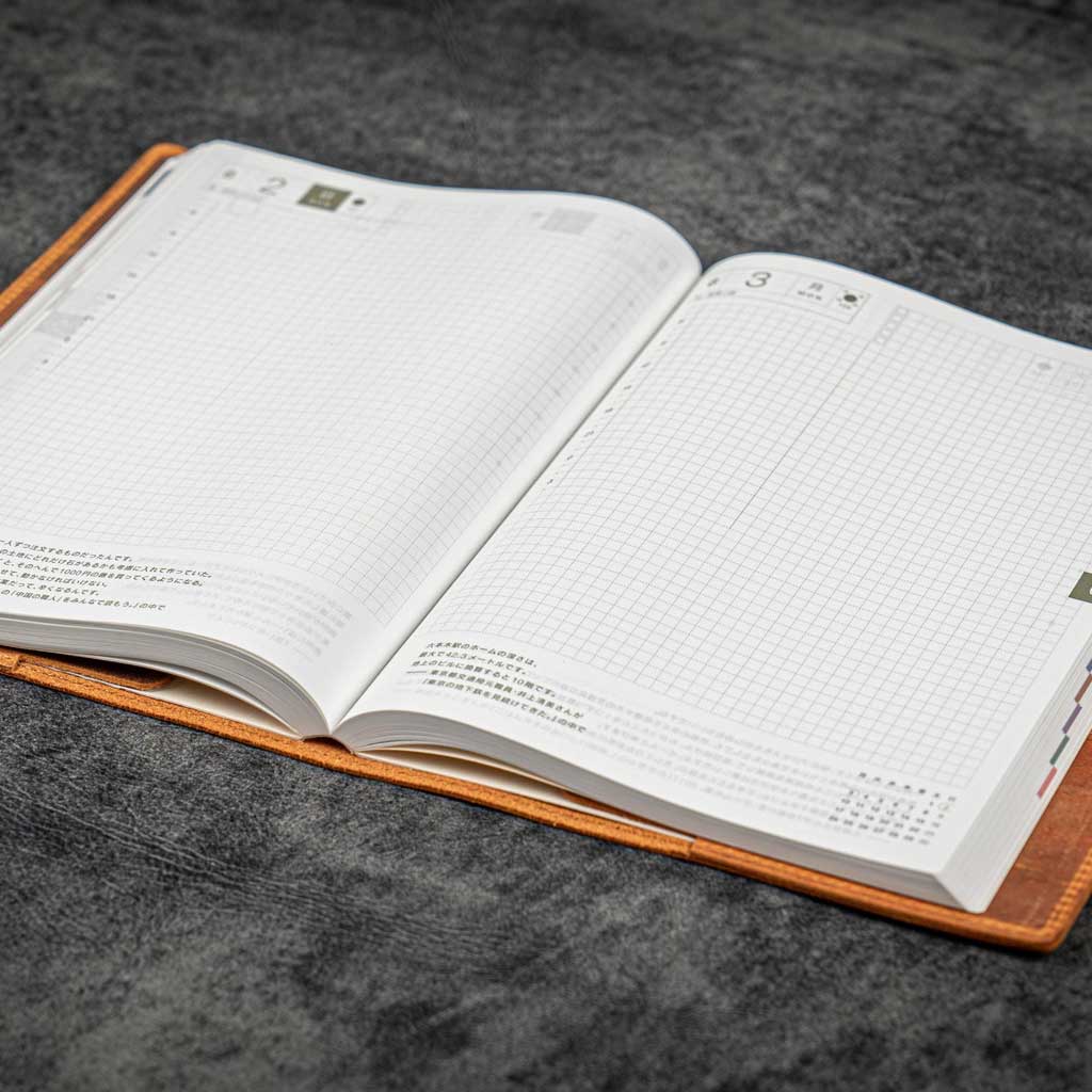 Open notebook with grid and text pages in brown leather notebook cover on a gray surface