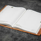 Open notebook with grid and text pages in brown leather notebook cover on a gray surface