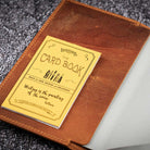 Brown leather notebook cover with yellow card on a textured surface