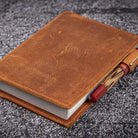 Brown leather notebook cover with pen holder on a textured surface