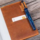 Brown leather notebook with a blue pen on a wooden surface