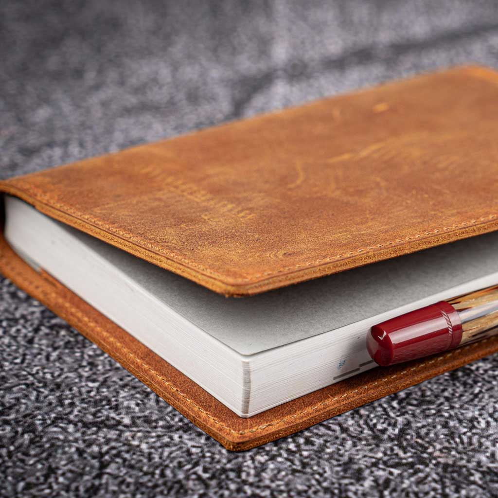 Brown leather notebook cover with a pen on a gray textured surface