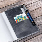 Fountain pen on a gray leather notebook cover with stamps on a wooden surface