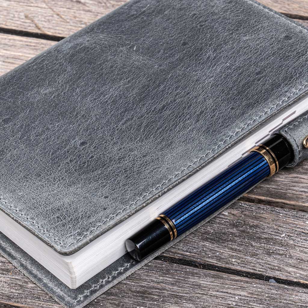 Gray leather notebook cover with a blue pen on a wooden surface