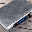 Gray leather notebook cover with a blue pen on a wooden surface