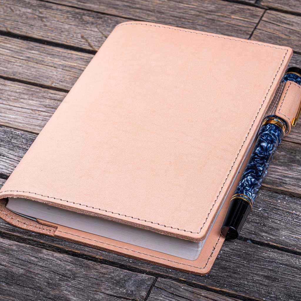 Natural undyed leather notebook with a pen holder on a wooden surface