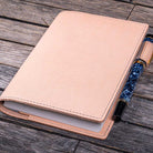 Natural undyed leather notebook with a pen holder on a wooden surface