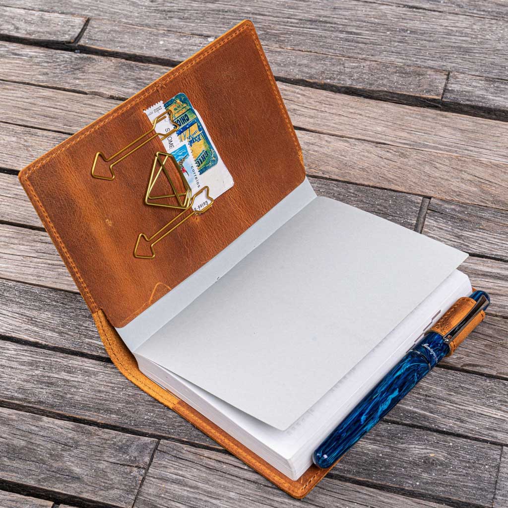 Open notebook with brown leather cover and pen and accessories on wooden surface