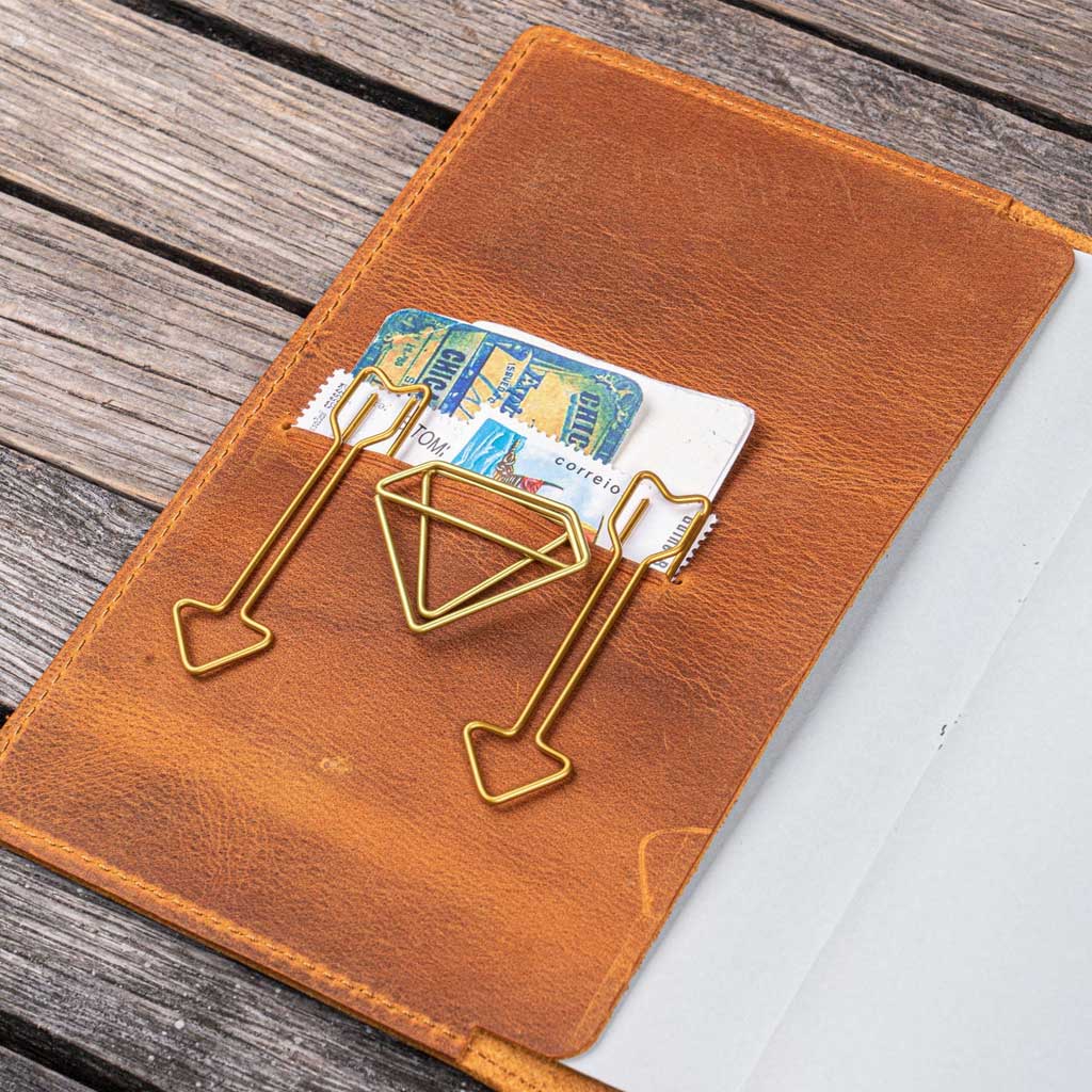 Three gold paper clips on a brown leather notebook with a card inside.