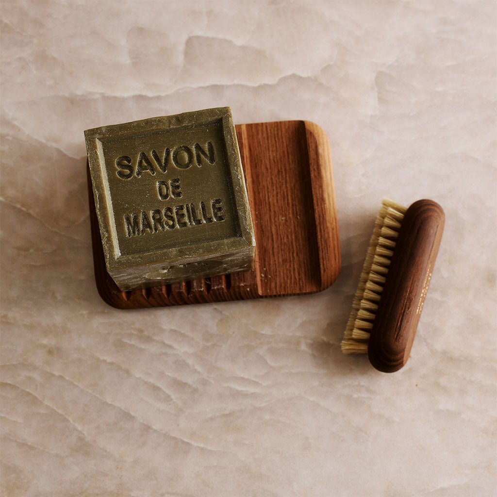 A wooden soap dish and nail brush with a cube of soap.
