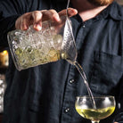 Person pouring a drink from a glass into a wine glass.