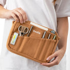 Person holding light brown canvas pouch with stationery supplies.