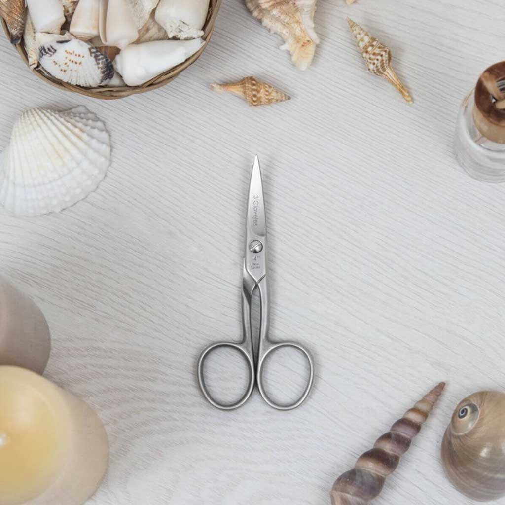 Nail scissors on textured background with seashells