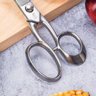Metal scissors on a textured surface with a wooden block and red object in the background