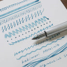 Kakimori stainless steel nib in metal dip pen with writing example in blue ink on white paper