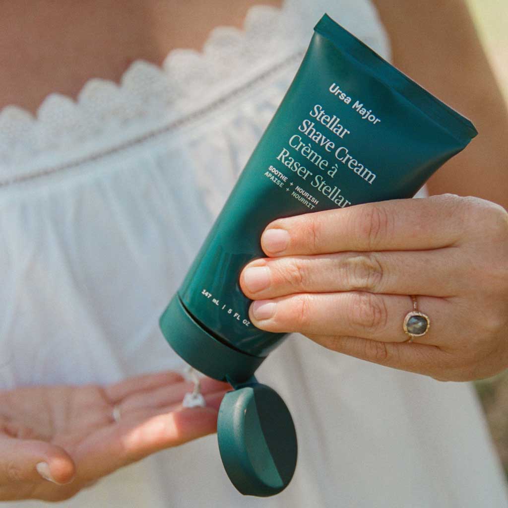 Person holding a green tube of Ursa Major Stellar Shave Cream with visible brand name.