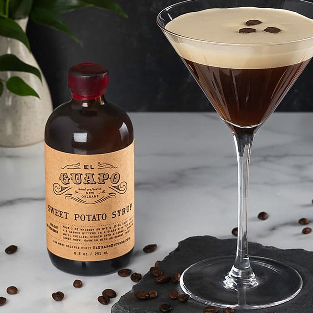 Bottle of El Guapo sweet potato syrup with a cocktail glass filled with a layered drink on a marble surface.