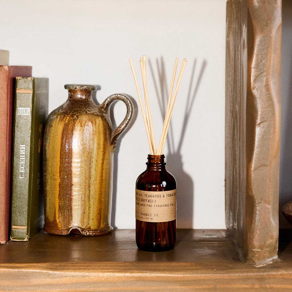 A bottle of diffuser with sticks and a ceramic pitcher on a wooden shelf.