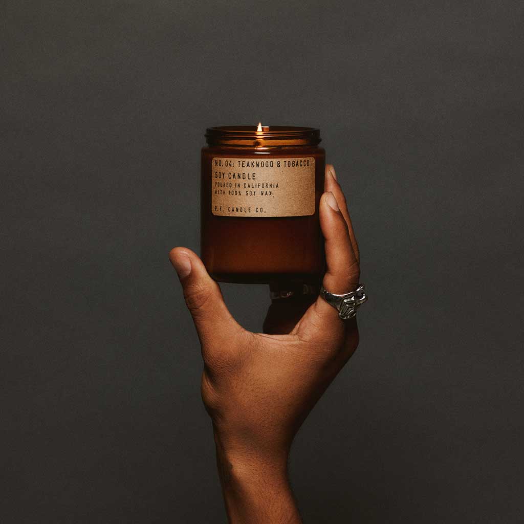 Hand holding a lit amber candle with a label against a dark background