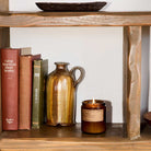 Wooden shelf with books, a ceramic pitcher, and a candle.