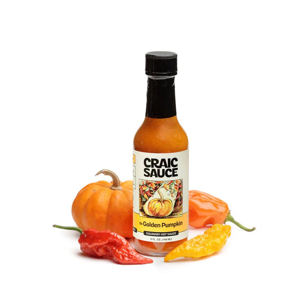 A bottle of Craic Sauce 'The Golden Pumpkin' seasoning hot sauce, styled with a small orange pumpkin and red, yellow, and orange peppers on a white background.