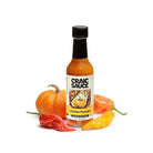 A bottle of Craic Sauce 'The Golden Pumpkin' seasoning hot sauce, styled with a small orange pumpkin and red, yellow, and orange peppers on a white background.