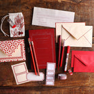 Red stationery and writing tools arranged on a wooden desk.
