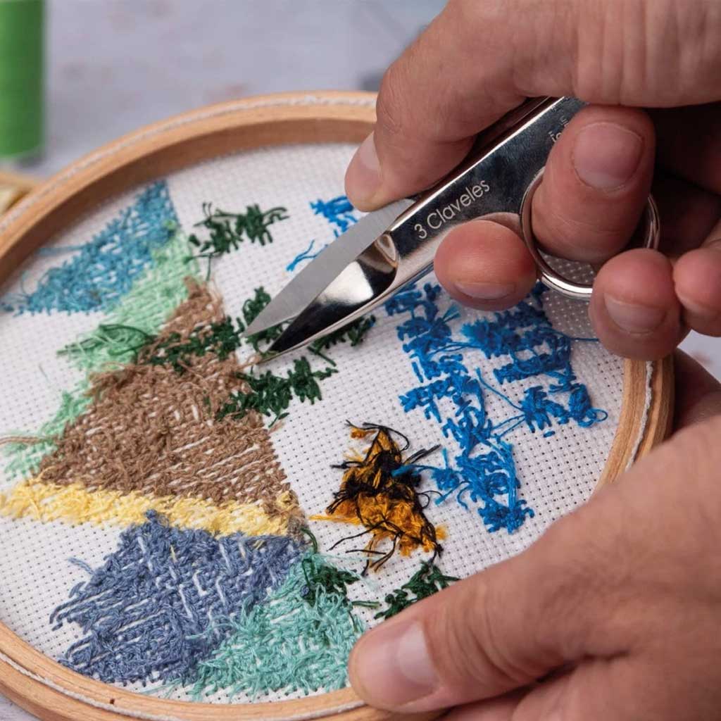Person using a pair of snips on an embroidery project with a mountain design.