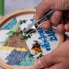Person using a pair of snips on an embroidery project with a mountain design.