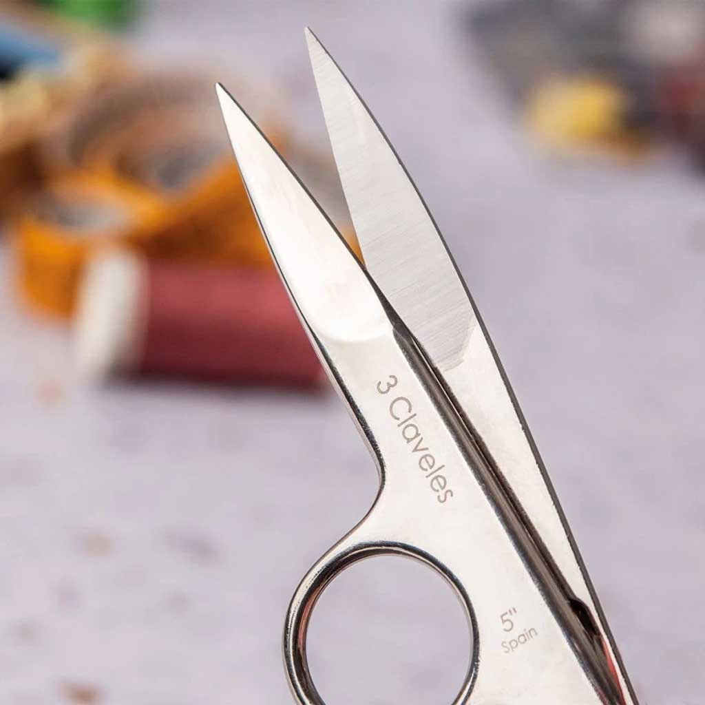 Pair of silver scissors with '3 Claveles' branding on a blurred background