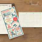 Traveler's Notebook plastic sheet board next to notebook on wooden table