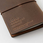 Brown leather notebook cover with embossed text that reads "20th traveler's notebook" on a white background