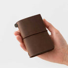 Hand holding brown card-size notebook against light background
