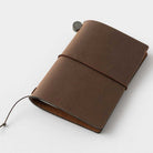 Closed brown card-size leather notebook on white surface