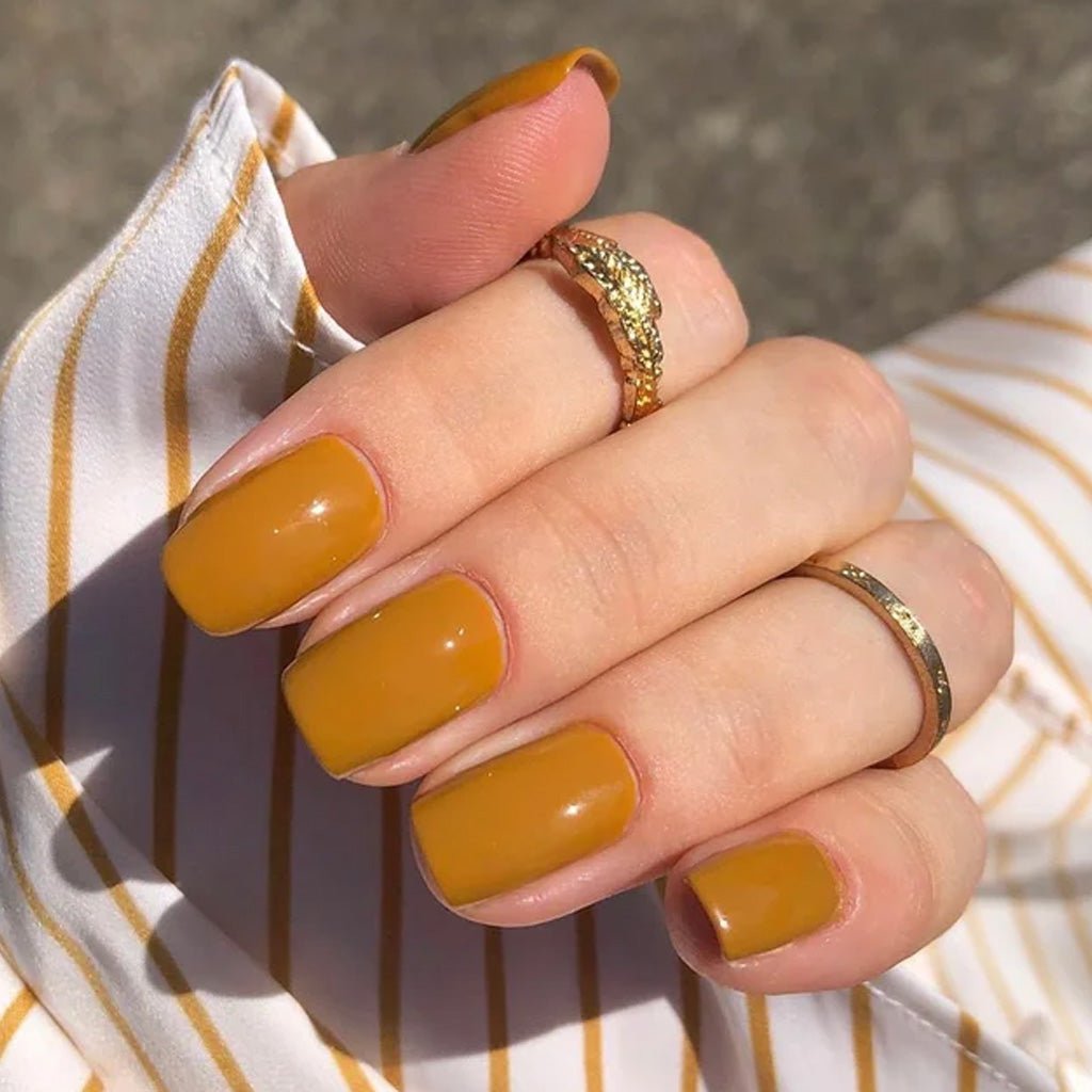 Hand wearing muted turmeric yellow nail polish