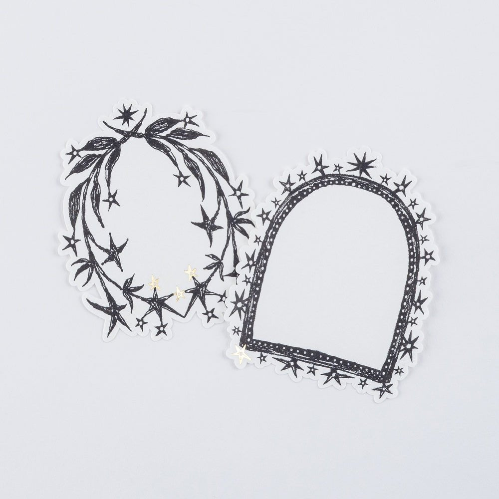Two decorative black and white stickers with stars and gold accents laying on white surface