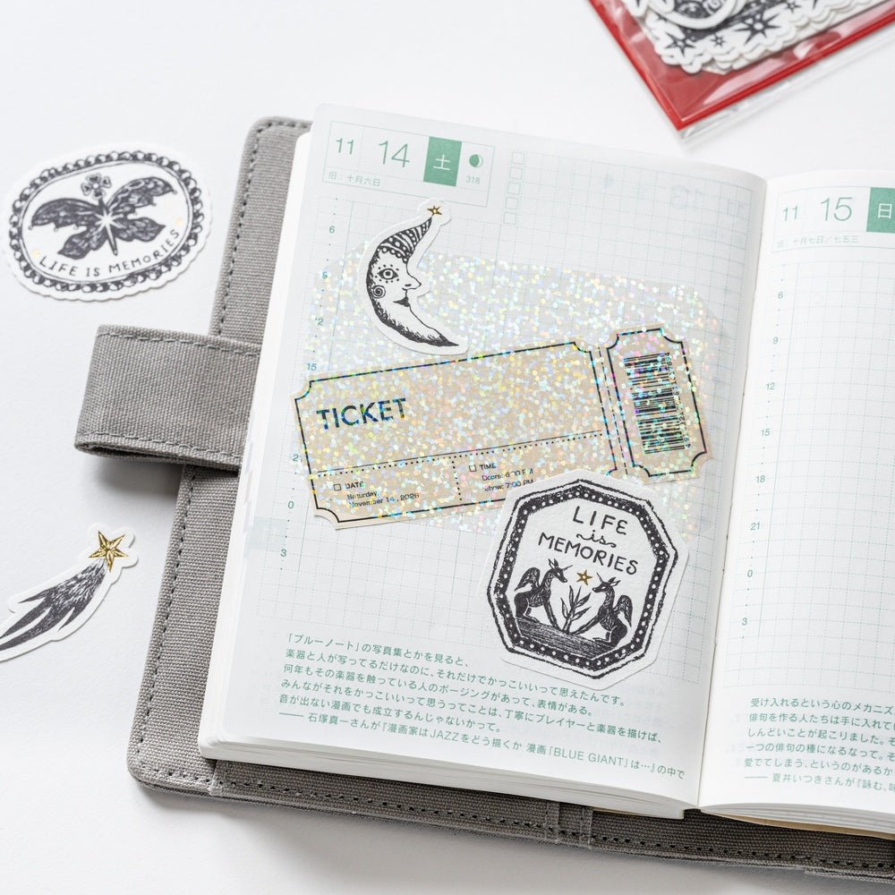 Open Hobonichi notebook with various black and white stickers and sparkly transparent layering sticker over page