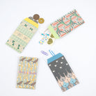 Set of four Hobonichi Unsodo mini paper envelopes with traditional Japanese woodblock print designs open and holding accessories and laying on white surface