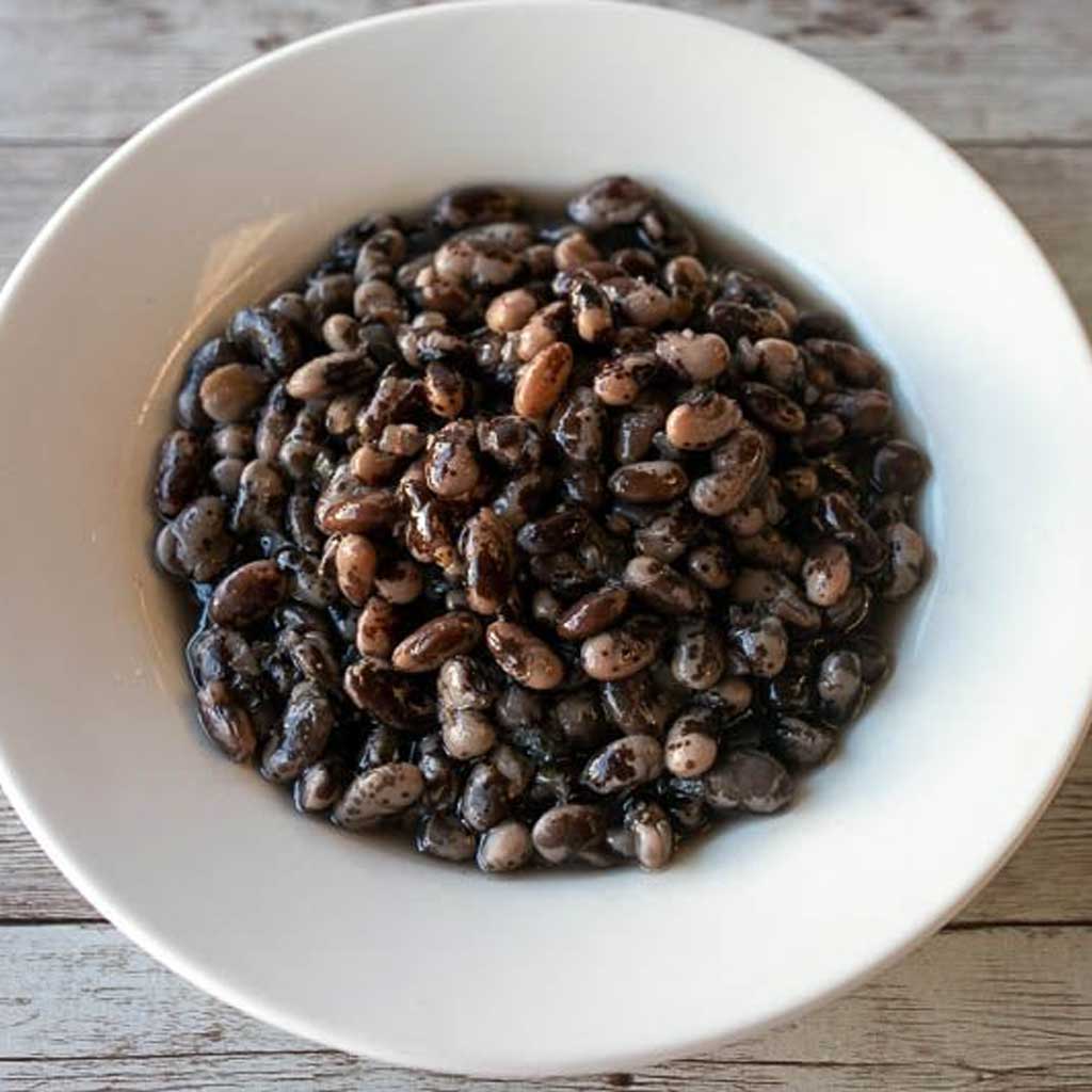 White bowl filled with black beans on a wooden surface