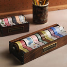 Wooden washi tape holder with colorful tapes and a cup of pencils in the background.