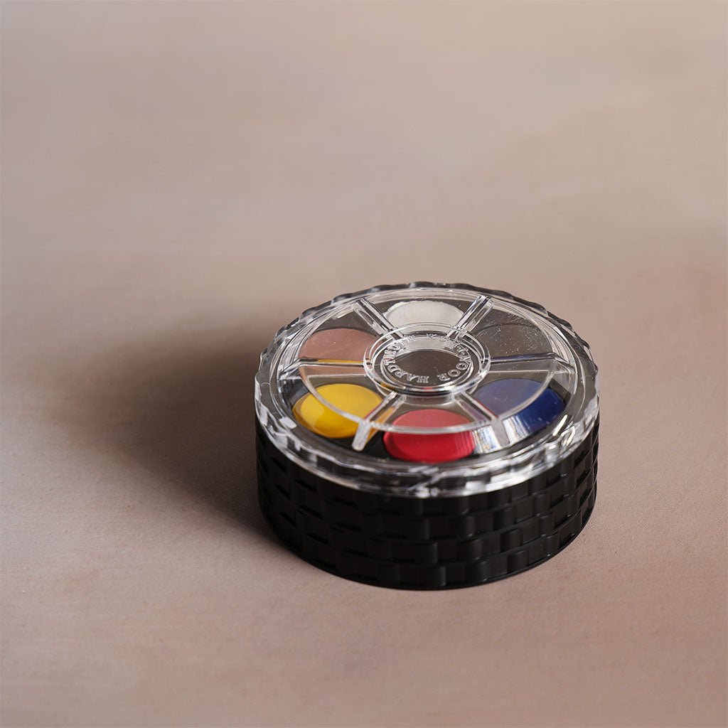 A stack of round plastic trays, each with six different colors of watercolor paint. A clear lid sits on top.