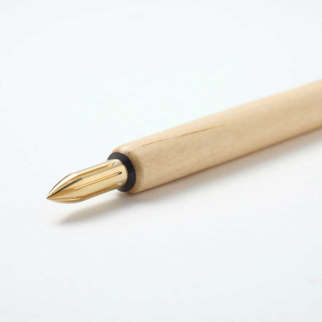White sakura wood nib holder with brass nib on white surface