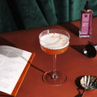 A whisky sour cocktail with a creamy foam head, in a coupe glass surrounded by cocktail making accessories. 