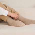 Hand pulling up beige knitted socks onto legs on light fabric couch
