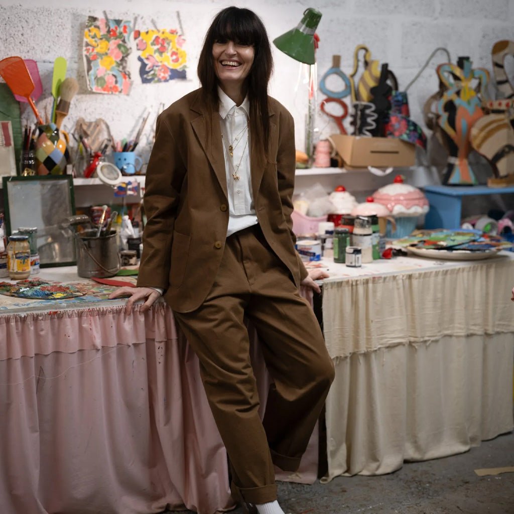 Person in a brown suit standing in an art studio with various art supplies and equipment.