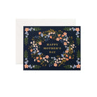 A Mother's Day greeting card with a floral pattern and 'Happy Mother's Day' text in the center on a navy blue background, accompanied by a soft white envelope.