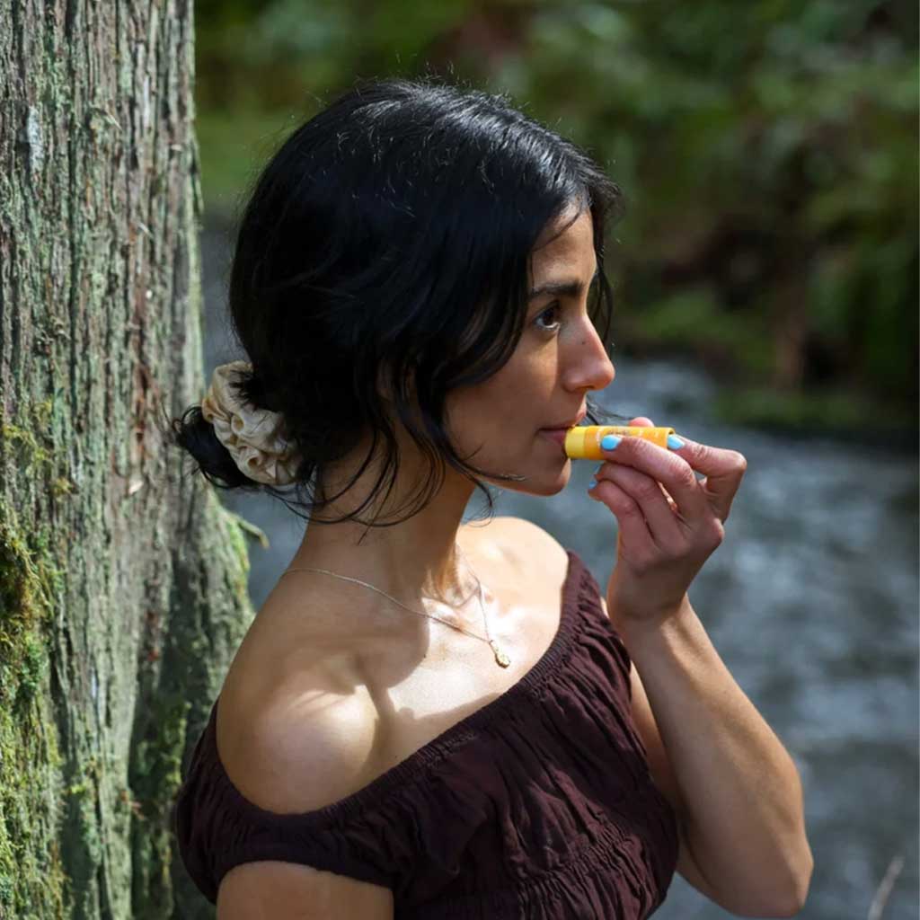 Woman applying hive lip balm against nature background