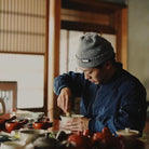 Person in a blue jacket and gray beanie working whisking matcha in bowl at a table.