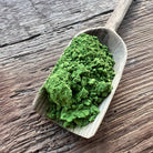 Wooden scoop filled with fine matcha powder on wooden surface