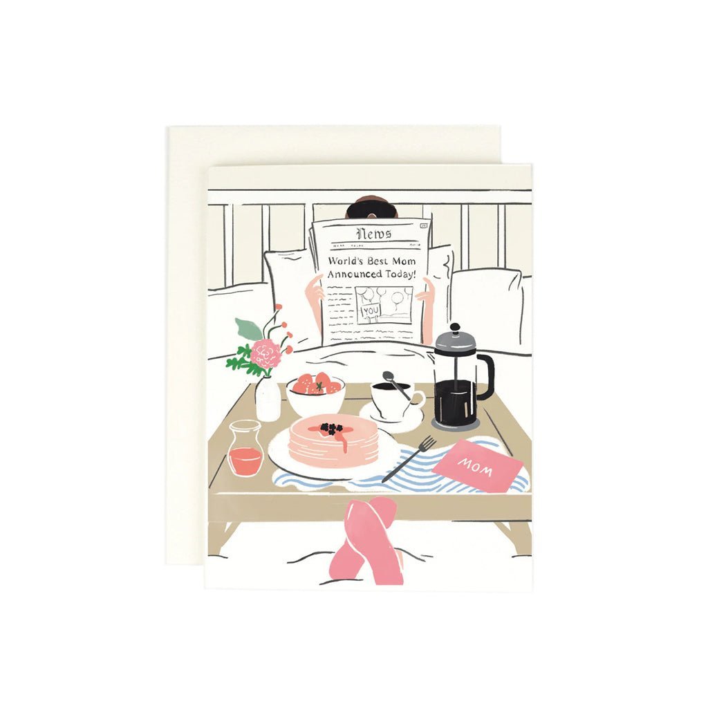 A greeting card depicting a cartoon of a newspaper with the headline 'World's Best Mom Announced Today', presented on a table with breakfast items and a pot of coffee.